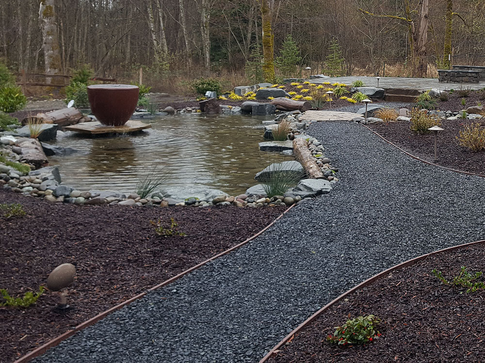 Tranquil Landscape Getaway - After: Low-maintenance backyard landscape design with fountain installation and paver patio
